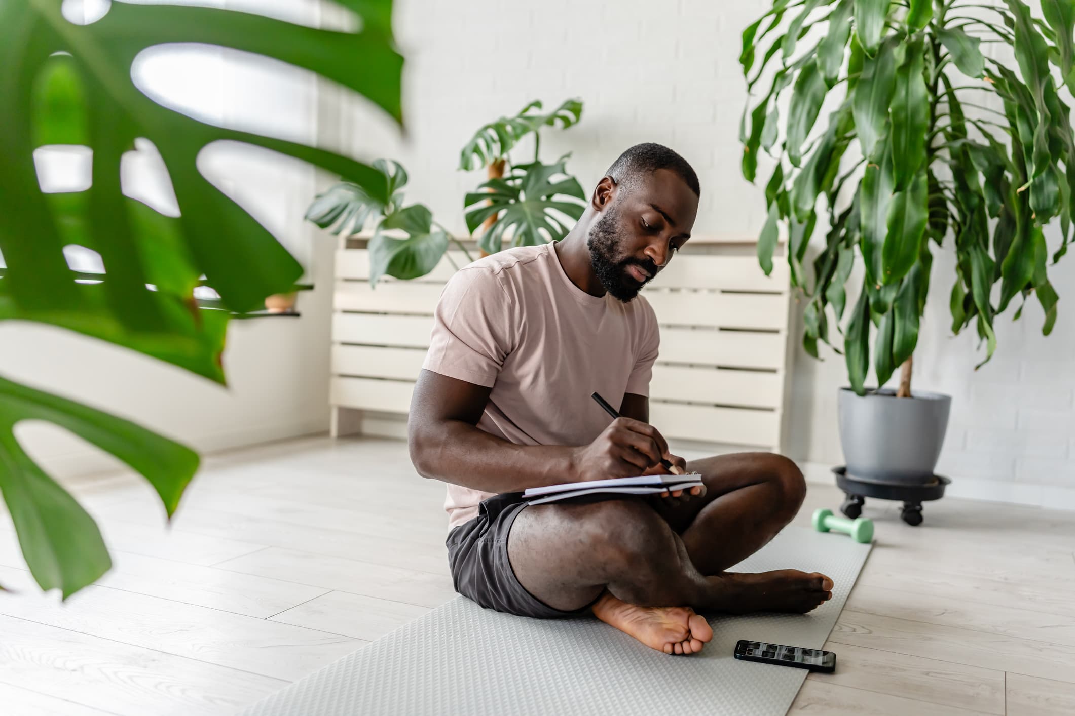 Man journaling on a yoga mat surrounded by plants
